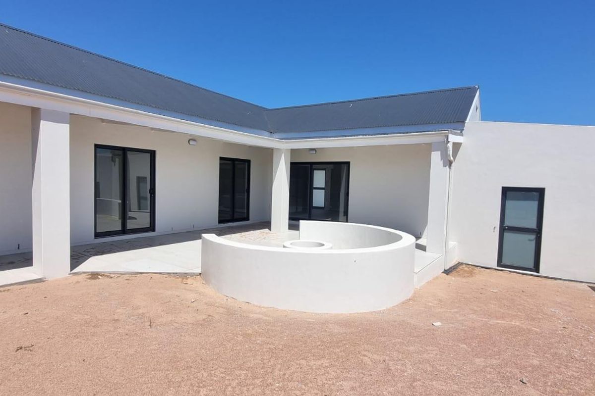 Rear exterior view featuring a covered patio, built-in circular fire pit, and modern sliding glass doors, set against a clean white facade.