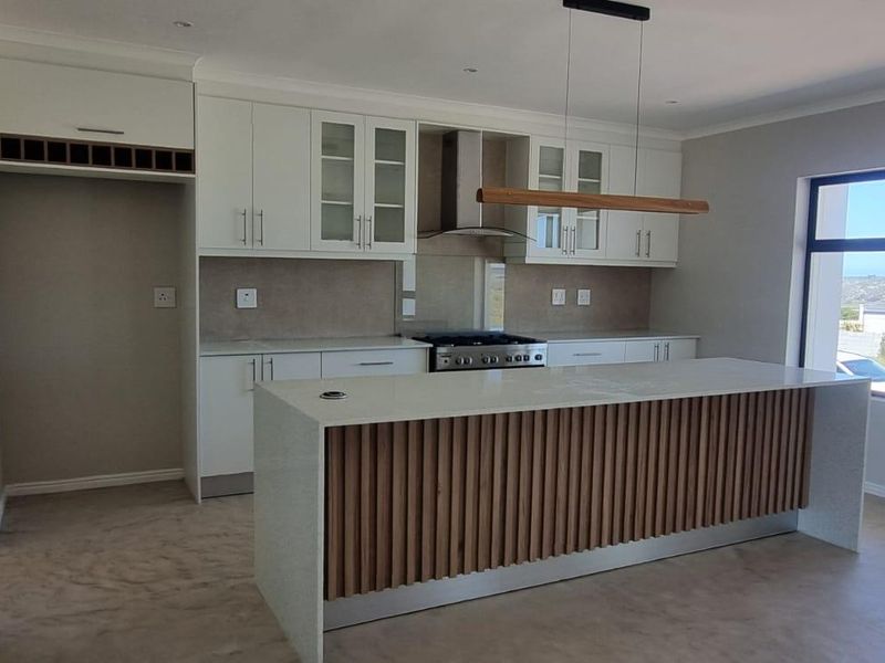 Modern kitchen featuring a large island with slatted wood detailing, stone countertops, built-in cabinetry, and high-quality stainless steel appliances.