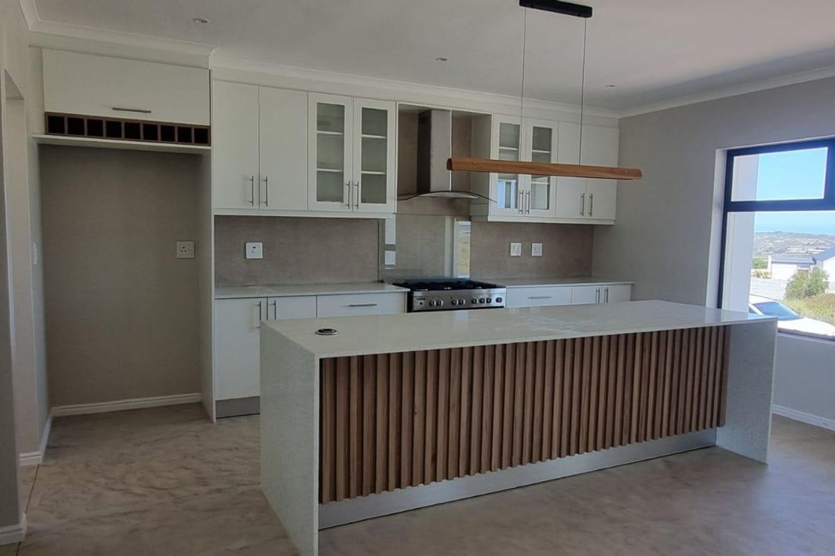 Modern kitchen featuring a large island with slatted wood detailing, stone countertops, built-in cabinetry, and high-quality stainless steel appliances.