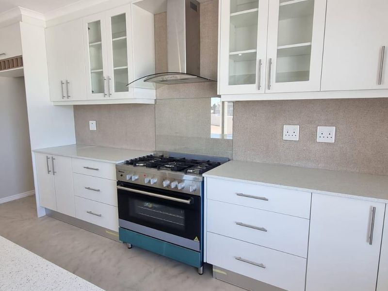 Modern kitchen featuring white cabinetry, stone countertops, a gas stove with extractor fan, and a neutral tiled splashback in a clean, open layout.