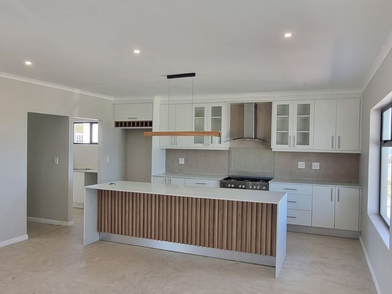 Modern open-plan kitchen featuring a central island with slatted wood detailing, white cabinetry, and integrated gas hob, seamlessly connected to a scullery area.