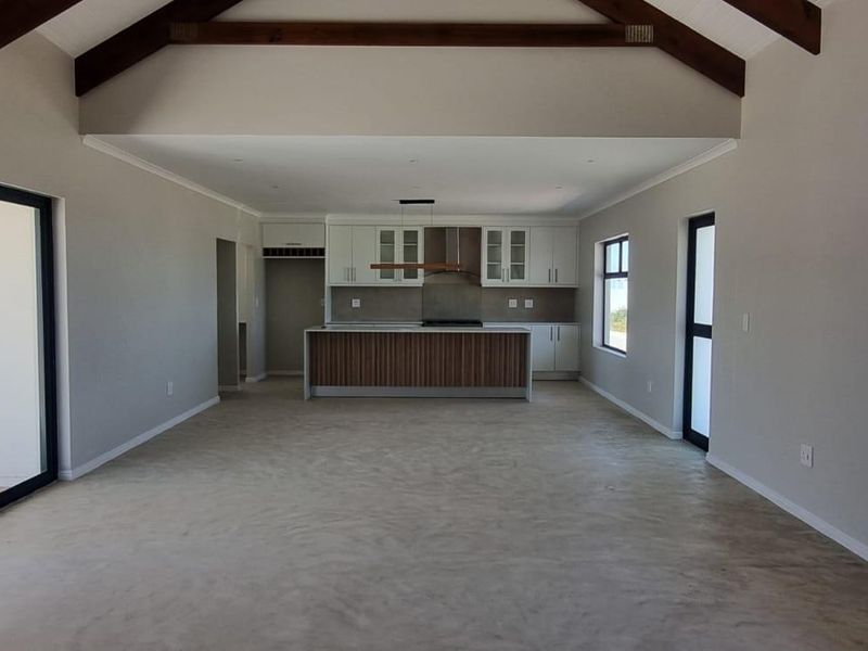 Spacious open-plan living and kitchen area featuring high vaulted ceilings with exposed timber beams, polished concrete floors, and modern built-in cabinetry.