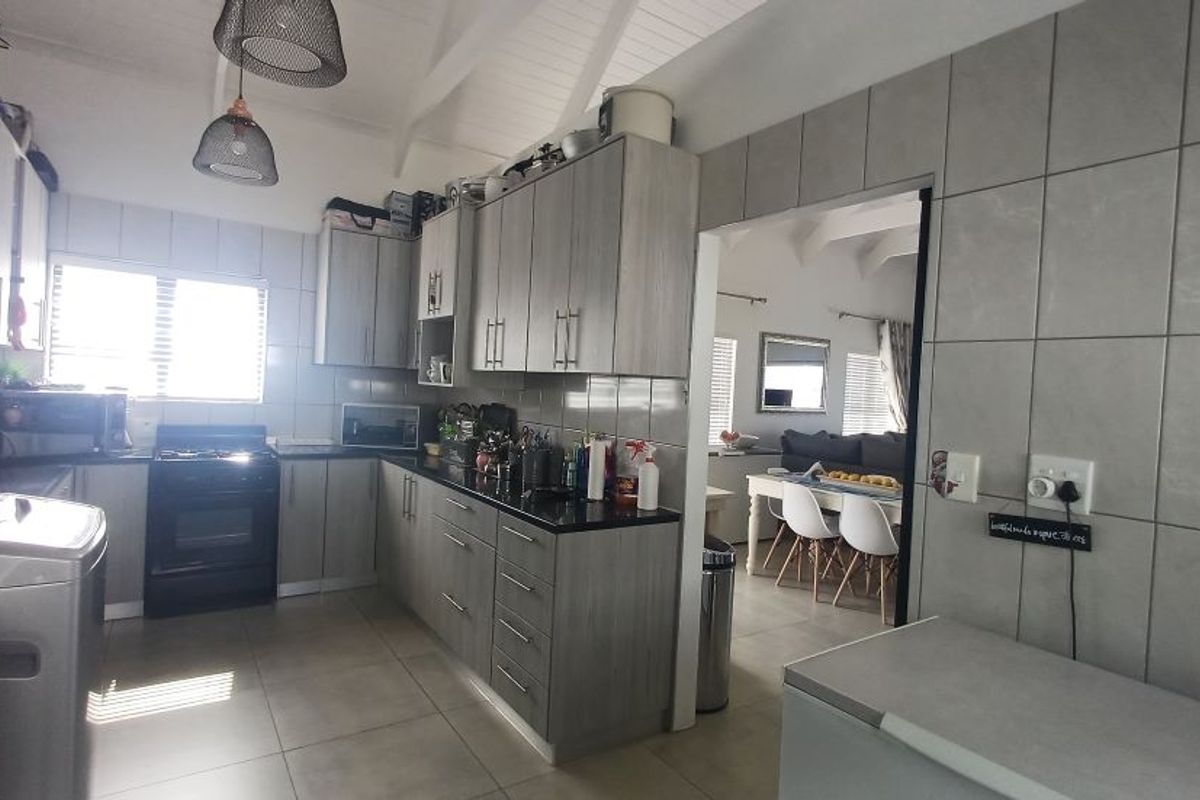 A functional kitchen featuring grey wood-look cabinetry, dark countertops, tiled walls, and a vaulted ceiling, with an open-plan flow into the dining area.