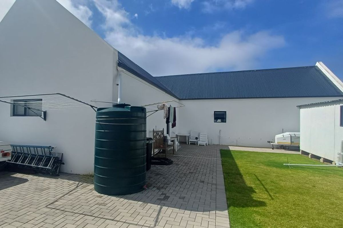 Rear exterior view of the property featuring a paved courtyard, lawn area, and a large water storage tank against the white building facade.