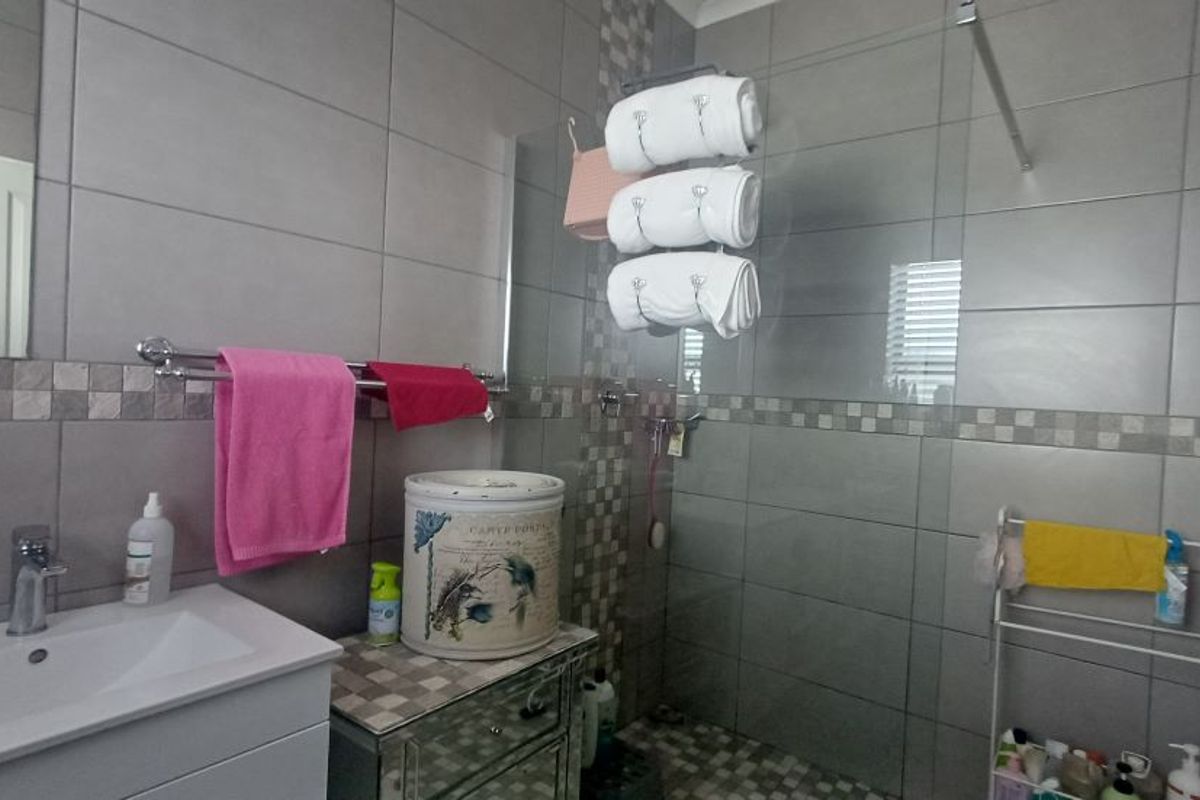 A modern bathroom featuring grey wall tiles, a glass shower enclosure, and a vanity basin with chrome fixtures.