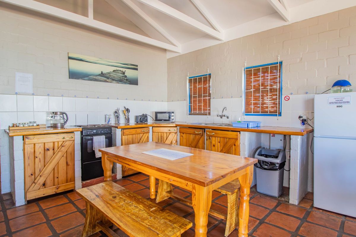 A rustic kitchen featuring wooden cabinetry, tiled countertops, exposed beam ceiling, and terracotta floor tiles, providing a functional and traditional workspace.