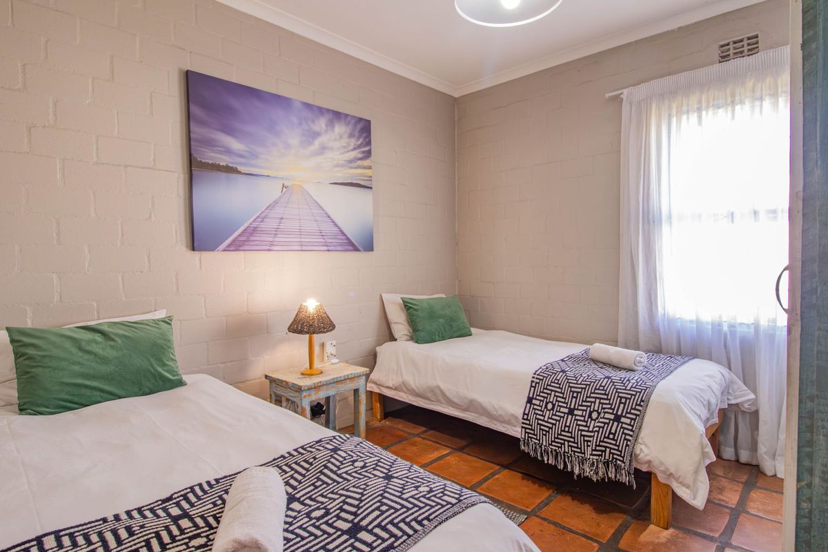 A bedroom featuring exposed brick walls, terracotta floor tiles, and a window with sheer curtains, providing a rustic and functional space.