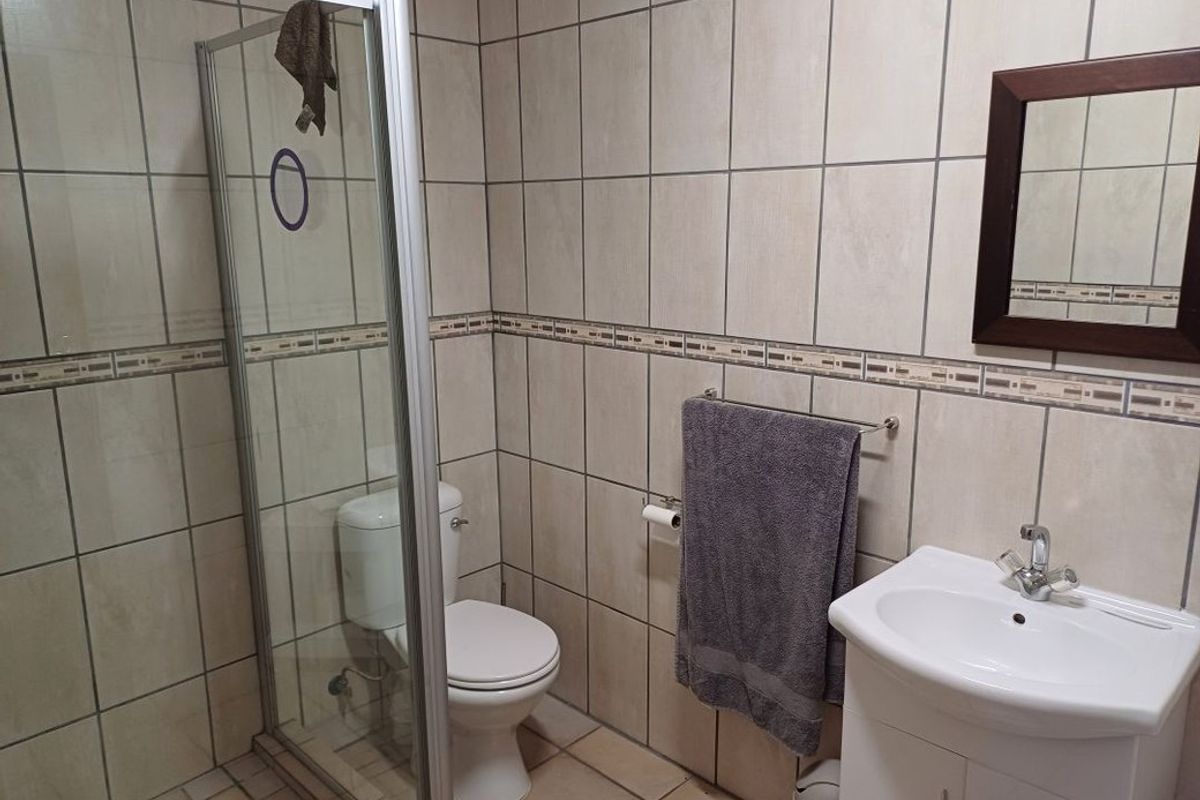 A functional bathroom featuring a glass shower enclosure, toilet, and a vanity basin with tiled wall and floor finishes.