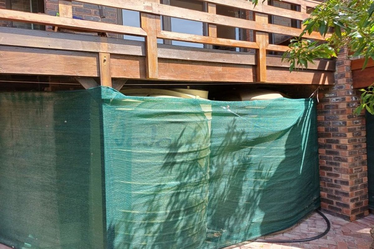 Rear exterior view showing a timber deck structure with a water storage tank concealed by shade cloth screening above a paved patio area.