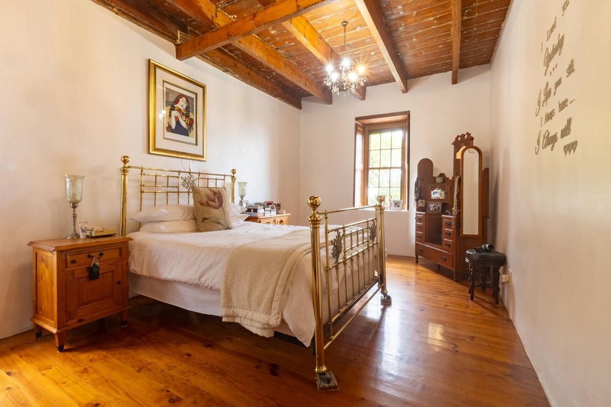 A rustic bedroom featuring exposed timber ceiling beams, polished wooden flooring, and a classic sash window.
