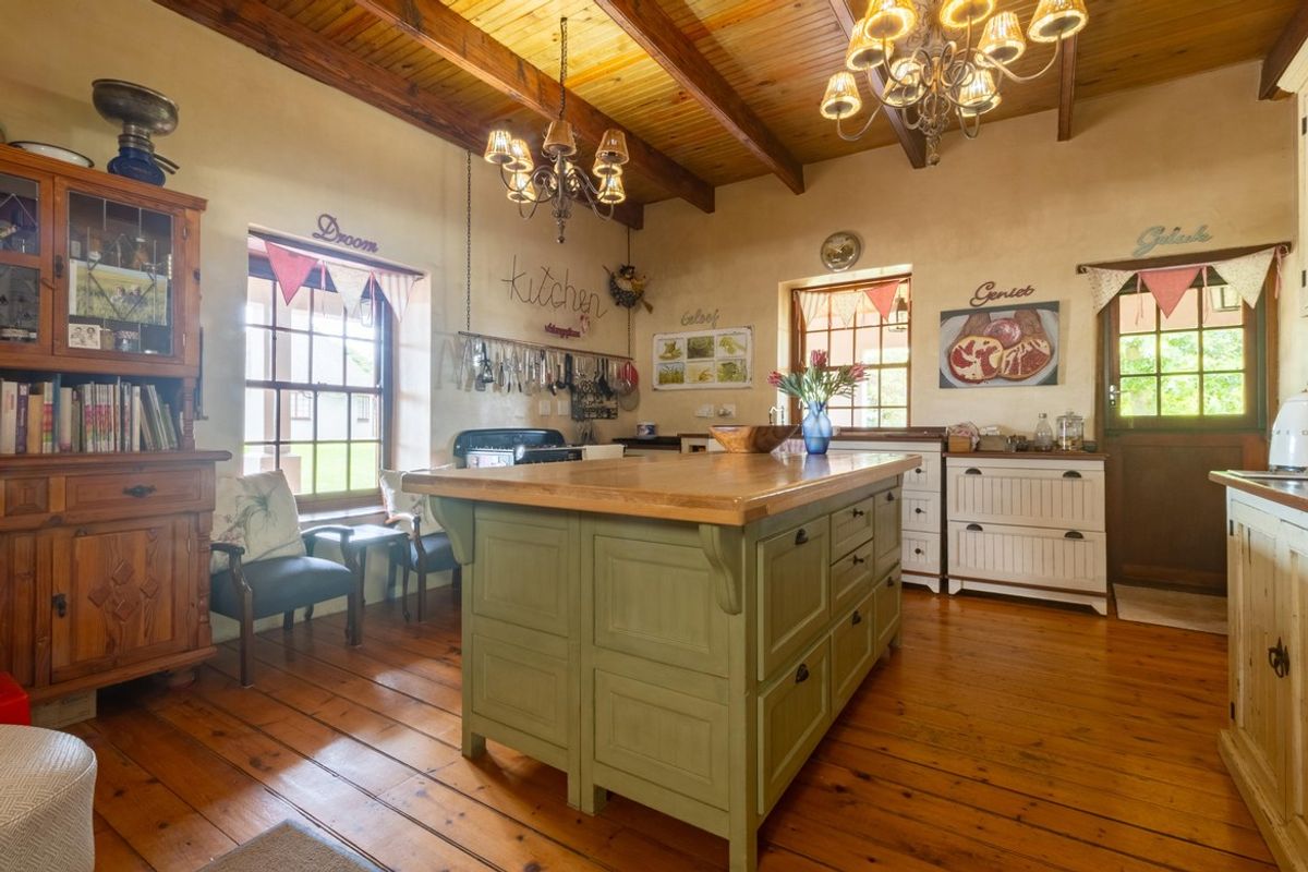 A rustic farmhouse kitchen featuring exposed timber ceiling beams, solid wood flooring, a large central kitchen island, and traditional sash windows.
