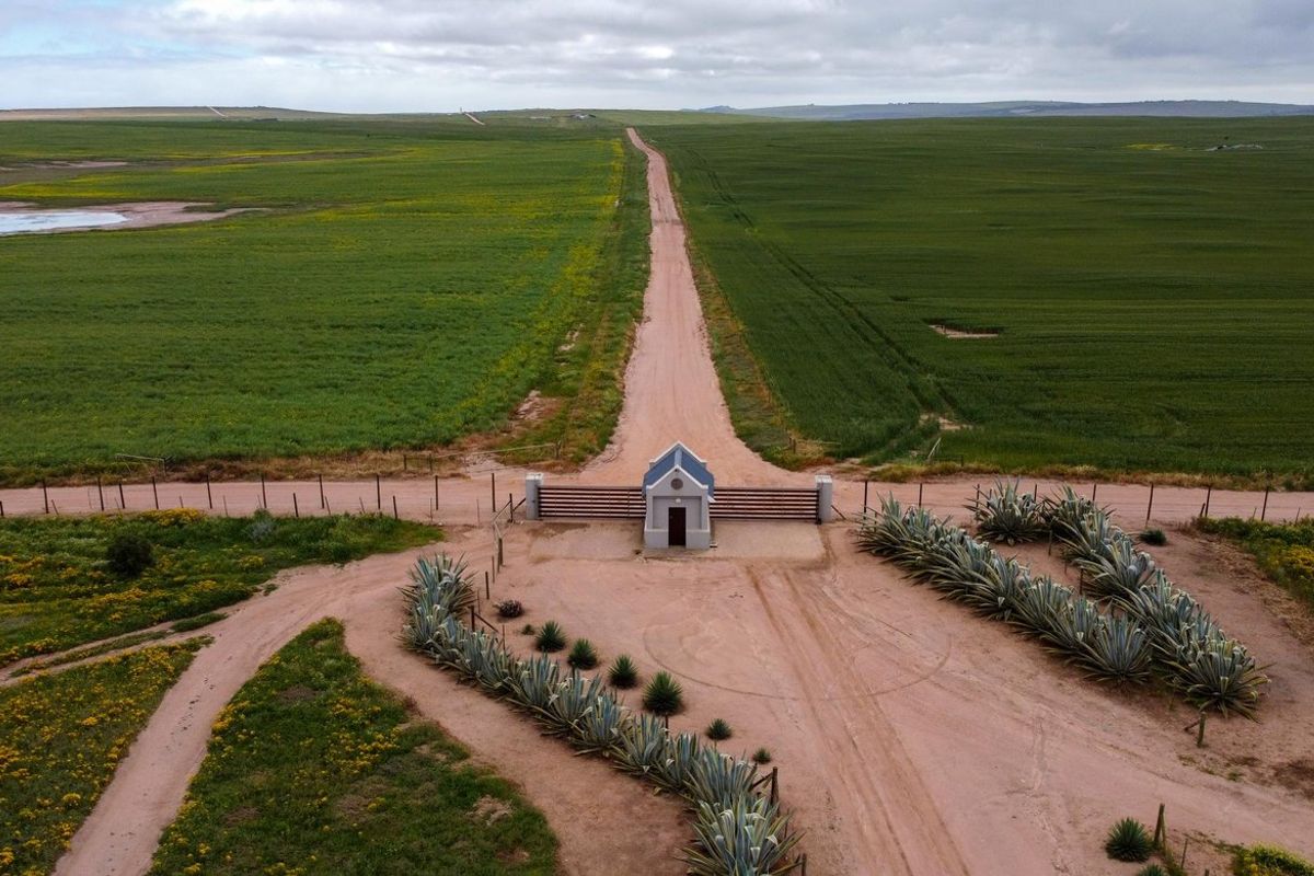 Aerial view of the farm entrance featuring a secure gated access point with a small guardhouse, set against expansive green agricultural fields.