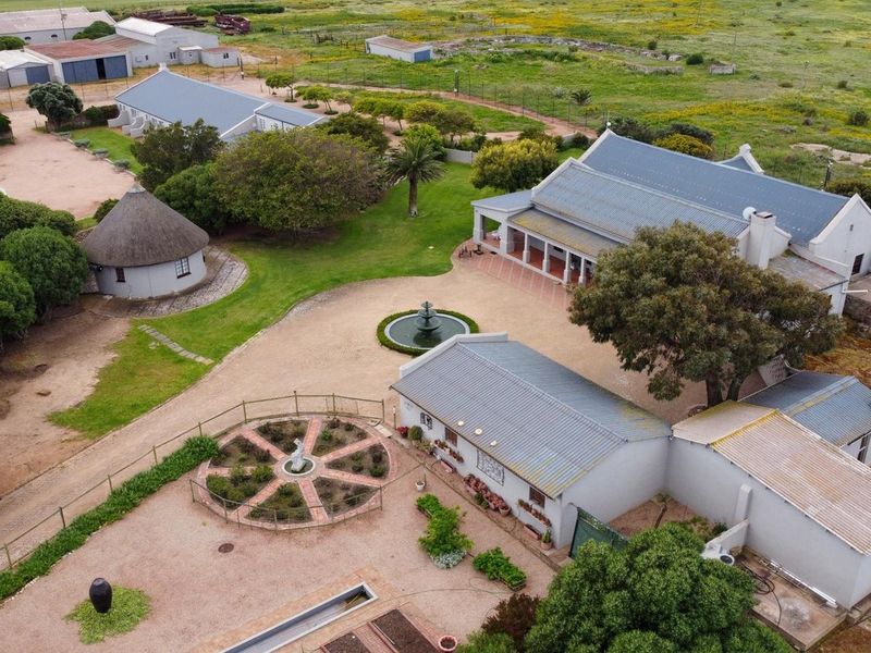 Aerial view of a farm property featuring multiple buildings, a central courtyard with a fountain, landscaped gardens, and surrounding agricultural land.