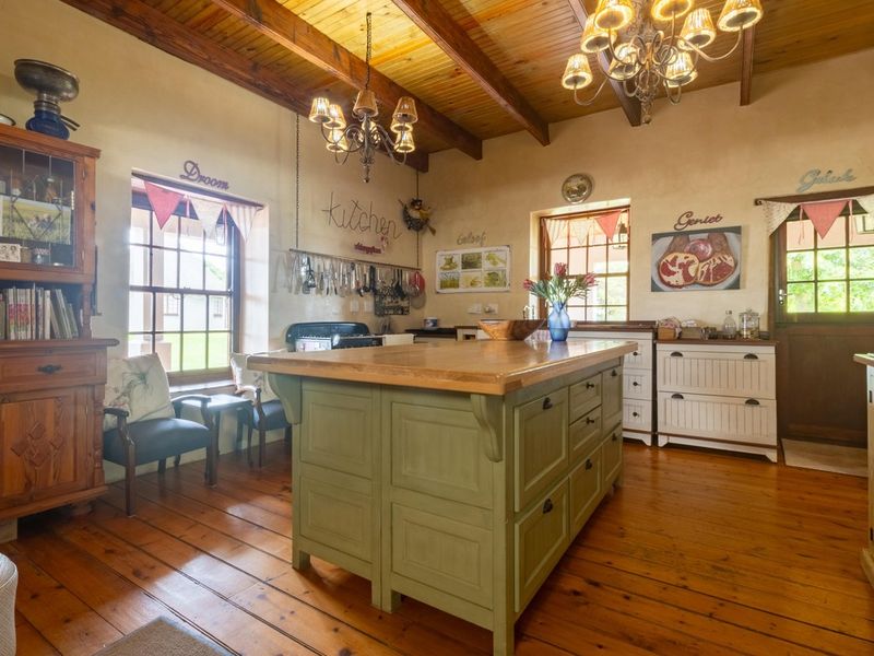 A rustic farmhouse kitchen featuring exposed timber ceiling beams, solid wood flooring, a large central kitchen island, and traditional sash windows.