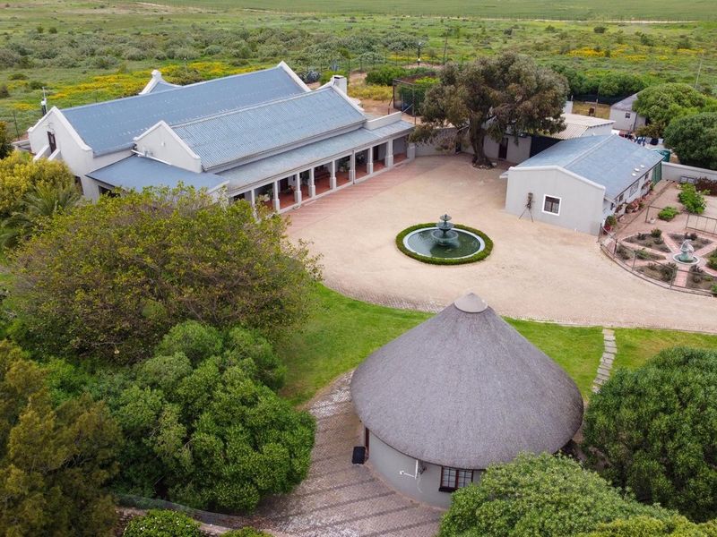 Aerial view of a farm property featuring a main residence with a covered veranda, a central courtyard with a fountain, and a thatched-roof outbuilding.