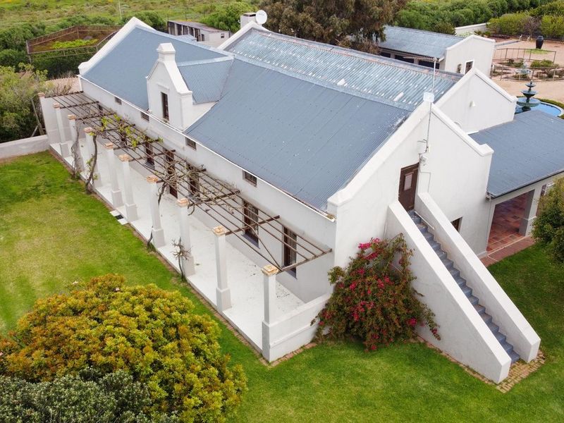 Aerial view of a traditional farm-style residence featuring a pitched metal roof, covered pergola patio, and external staircase set within a landscaped garden.