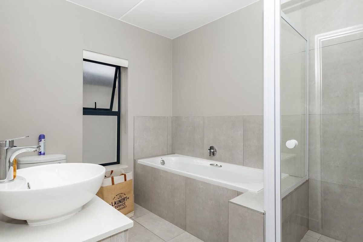Modern bathroom featuring a white vessel sink, a built-in bathtub with neutral tiling, and a separate glass-enclosed shower.