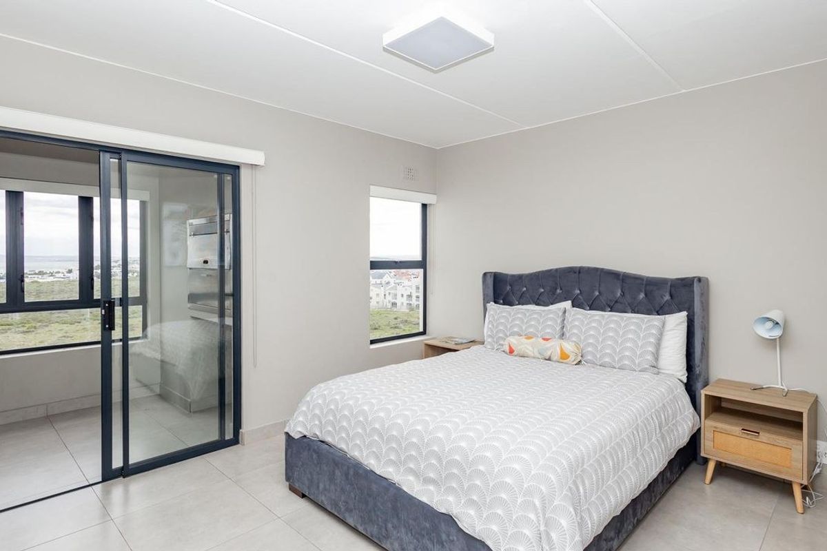 A bright bedroom featuring neutral tiled flooring, large windows, and a sliding glass door leading to a balcony with scenic views.