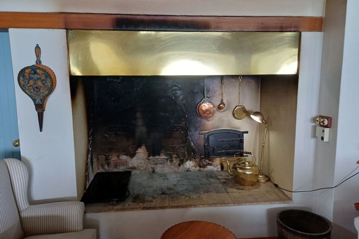 A traditional living room featuring a large masonry fireplace with a prominent brass hood and integrated oven door, showing significant signs of soot accumulation.