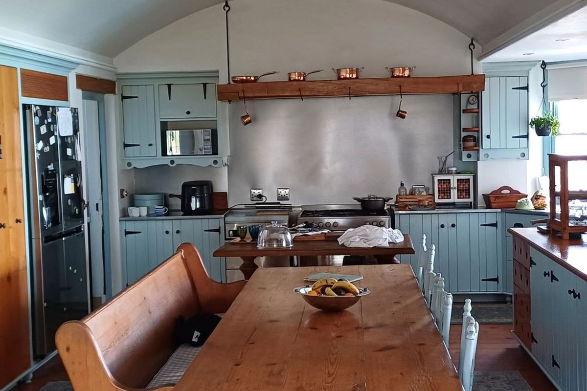 A charming country-style kitchen featuring light blue cabinetry, a stainless steel splashback, a gas range, and a distinctive vaulted ceiling.