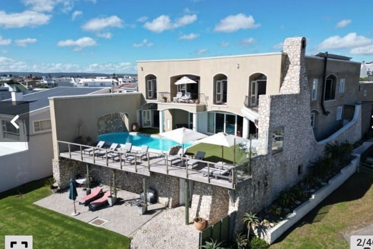 Aerial view of a multi-level residence featuring a swimming pool, raised timber deck, stone facade, and landscaped garden areas.