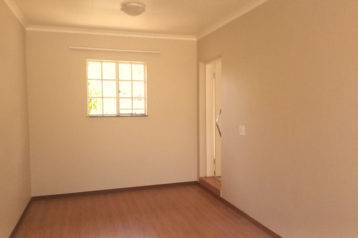 A clean, empty bedroom featuring laminate flooring, neutral walls, and a window providing natural light.