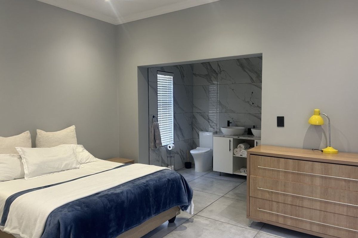 Spacious bedroom featuring an open-plan en-suite bathroom with modern marble-look tiling, dual vanity, and a private toilet area.