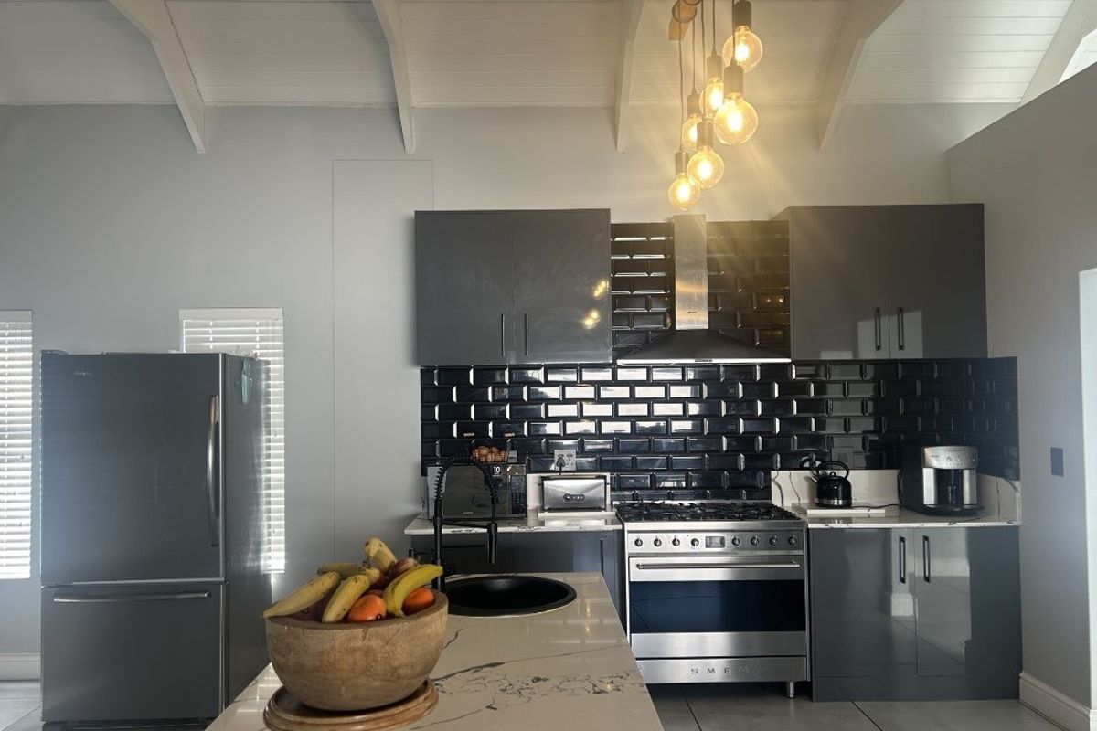 Modern kitchen featuring dark grey cabinetry, black subway tile backsplash, stone countertops, a central island, and a stainless steel gas range with extractor fan.