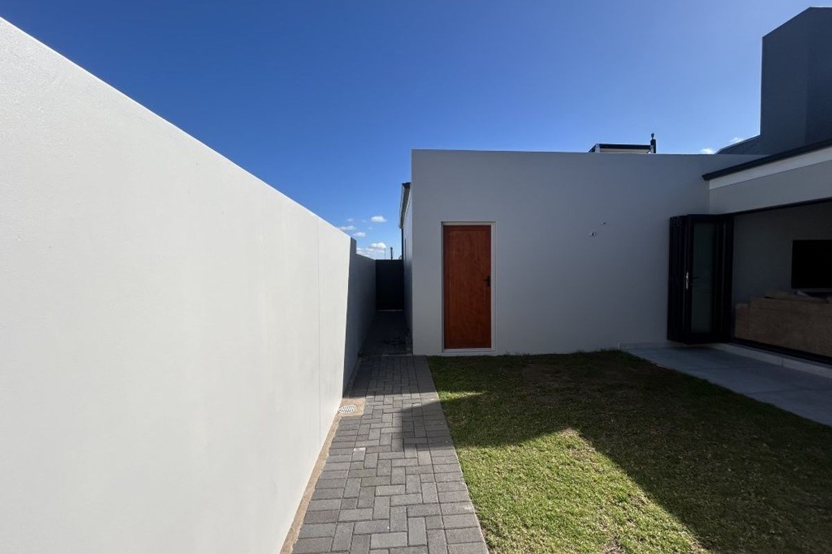 A view of the rear exterior area featuring a paved walkway, a small lawn, and a side access door leading to the property.