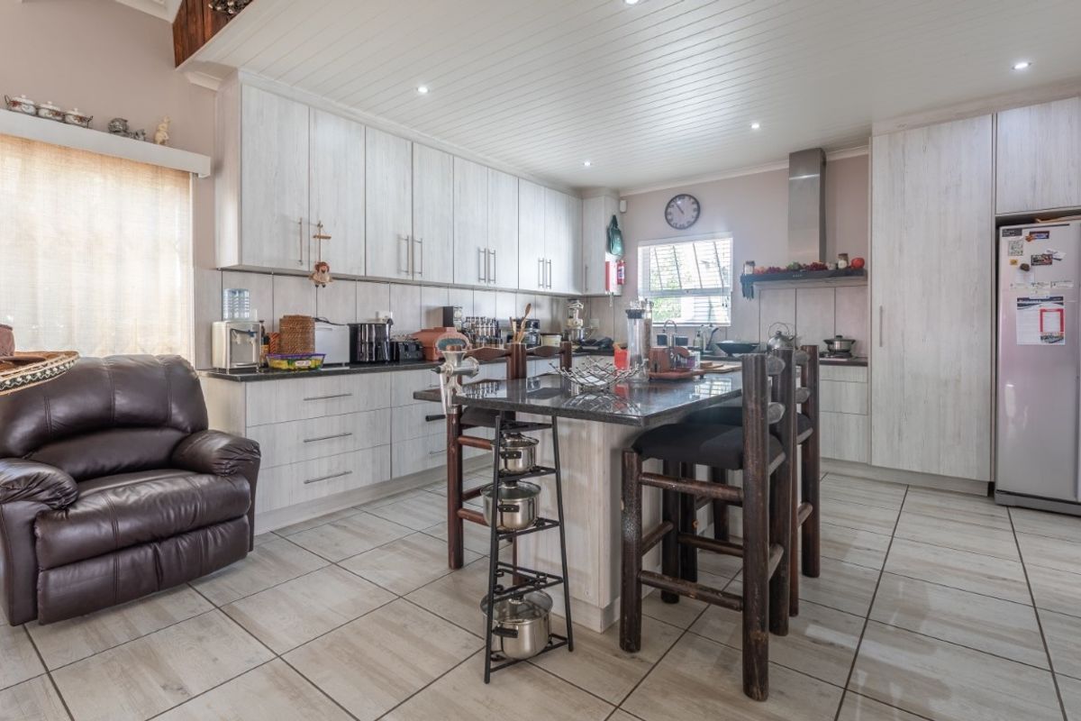 A spacious kitchen featuring light wood-grain cabinetry, a central island with stone countertops, tiled flooring, and recessed ceiling lighting.