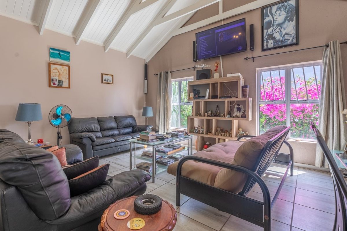 Spacious living room featuring high vaulted ceilings with exposed beams, tiled flooring, and large windows allowing for ample natural light.
