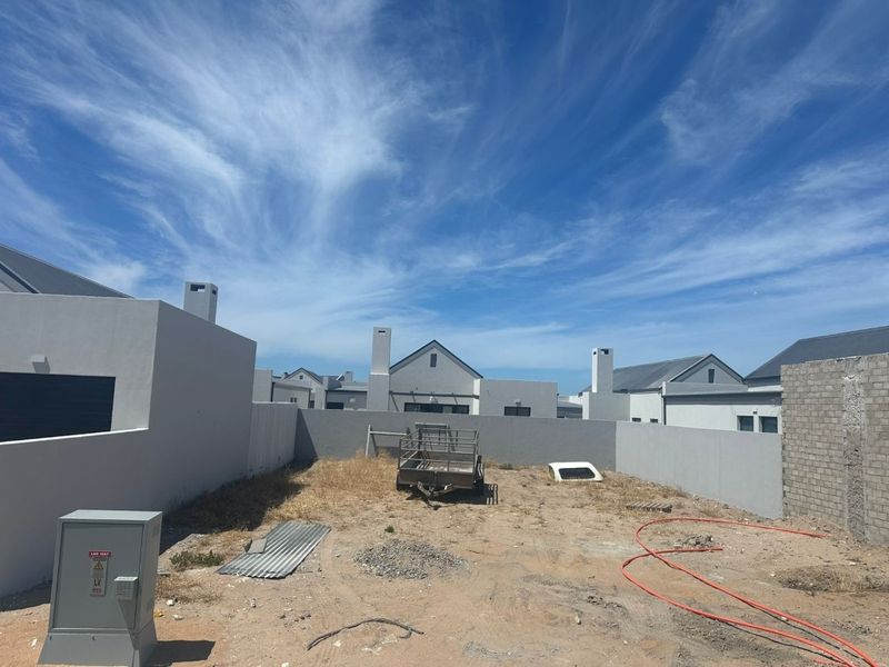 A rear yard area featuring boundary walls and an electrical distribution box, currently awaiting landscaping and final site completion.