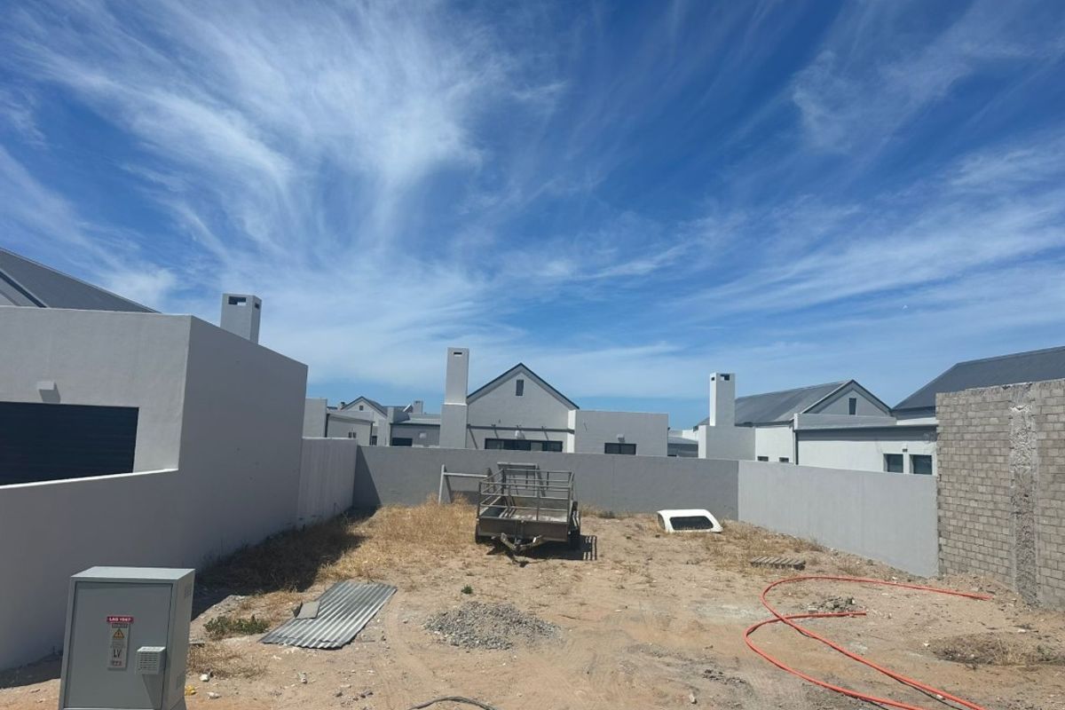 A rear yard area featuring boundary walls and an electrical distribution box, currently awaiting landscaping and final site completion.