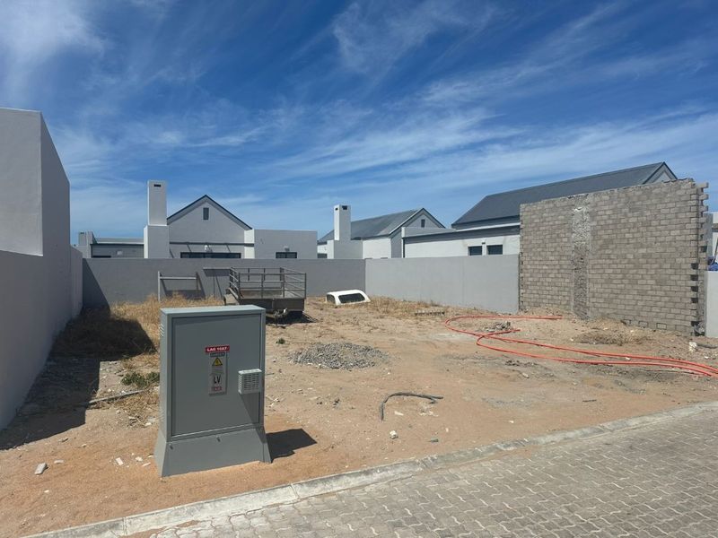 An undeveloped rear yard area featuring boundary walls, an electrical utility box, and unfinished ground surfaces ready for landscaping.