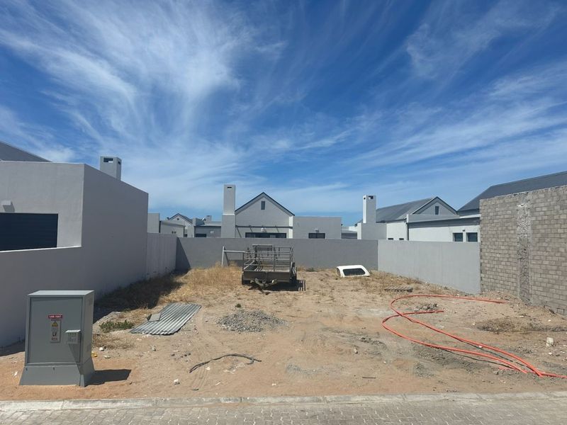 An undeveloped rear plot featuring boundary walls, an electrical distribution box, and unlandscaped ground, offering a blank canvas for garden design.