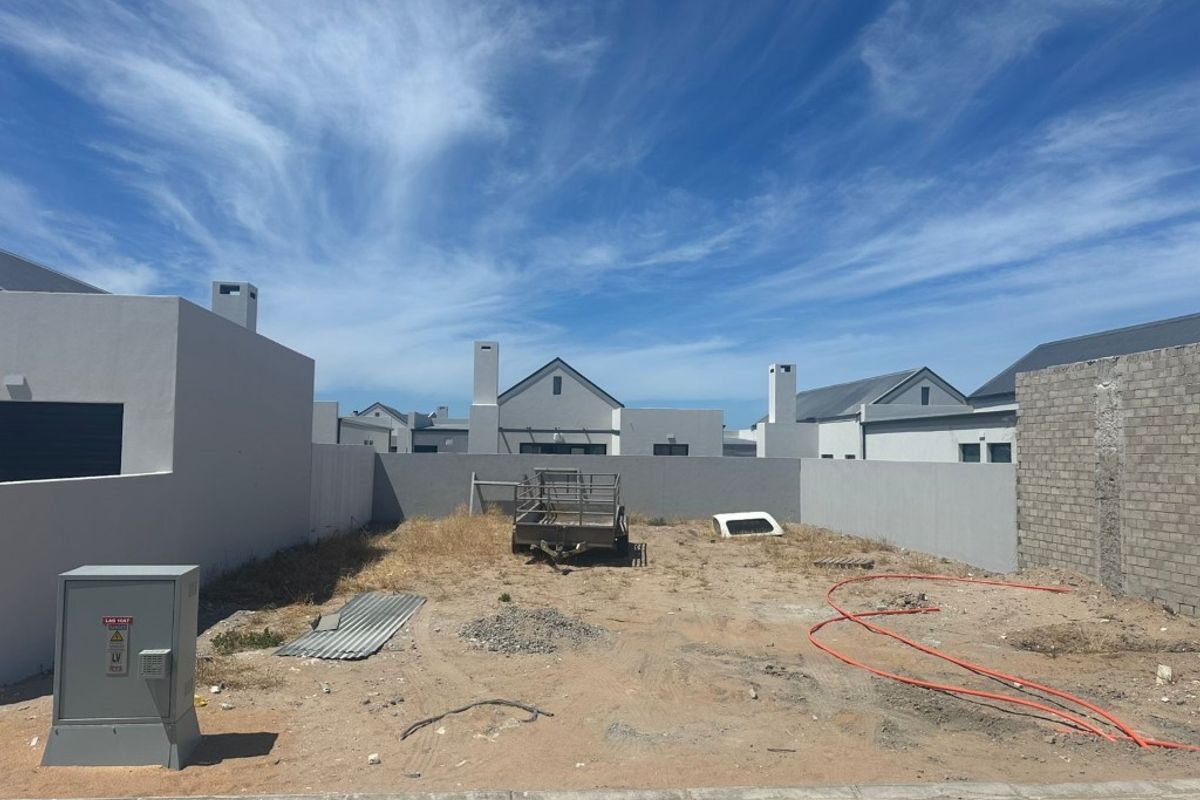 An undeveloped rear plot featuring boundary walls, an electrical distribution box, and unlandscaped ground, offering a blank canvas for garden design.