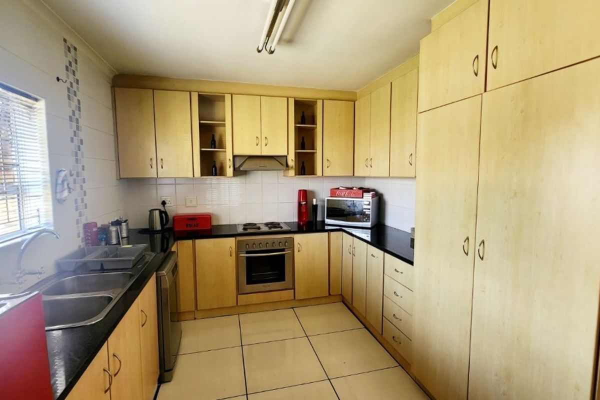 A functional kitchen featuring light wood-toned cabinetry, black countertops, a built-in oven, hob, and extractor fan with tiled flooring.