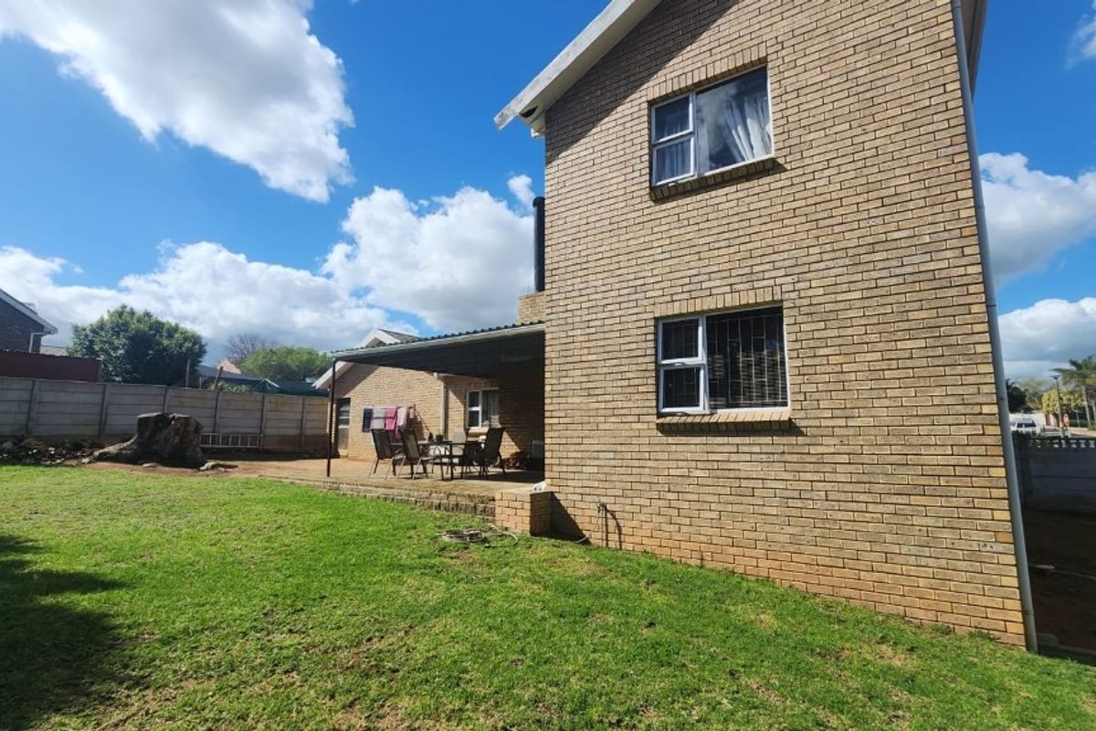 Rear view of a double-story brick house featuring a covered patio area and a spacious backyard.