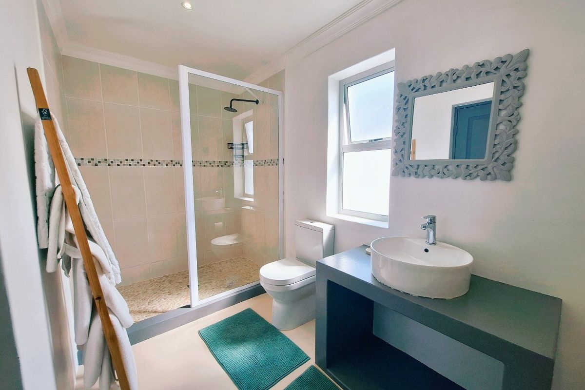 A modern bathroom featuring a walk-in shower with pebble-style flooring, a contemporary vessel sink on a vanity unit, and a toilet.