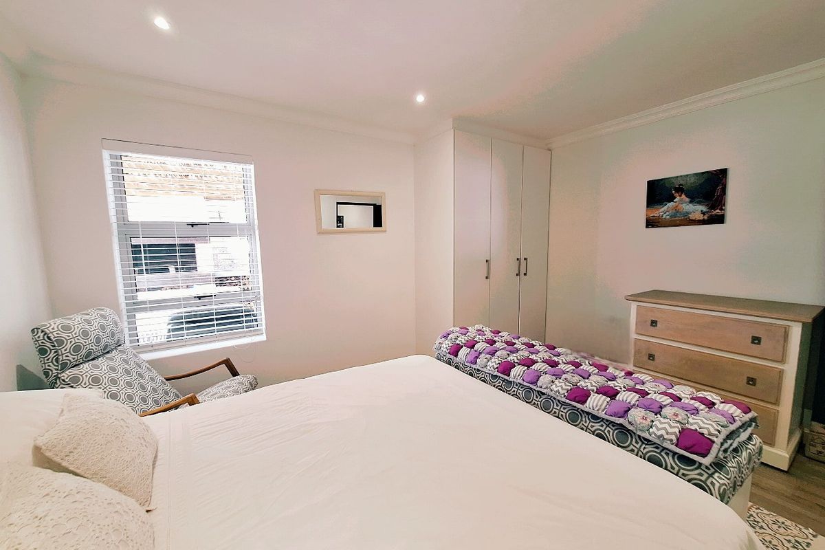 A well-maintained bedroom featuring built-in cupboards, recessed ceiling lighting, and a window with fitted blinds.