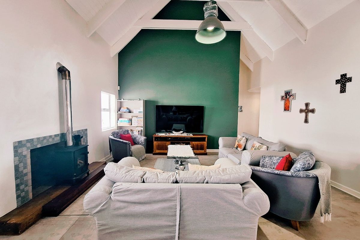 Spacious living room featuring a high vaulted ceiling with exposed beams, a prominent green feature wall, and a built-in wood-burning fireplace.