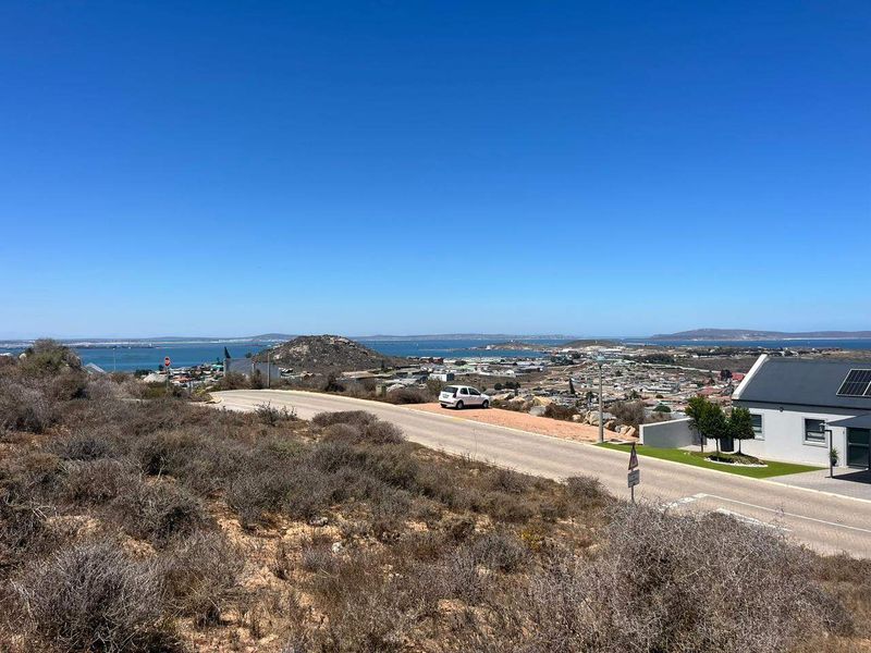 Elevated view overlooking the coastal town, surrounding landscape, and ocean horizon from the vacant residential plot.