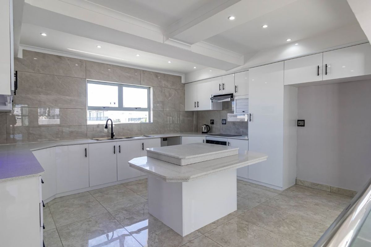 Modern kitchen featuring high-gloss white cabinetry, stone countertops, a central island, integrated extractor fan, and large-format polished floor tiles.