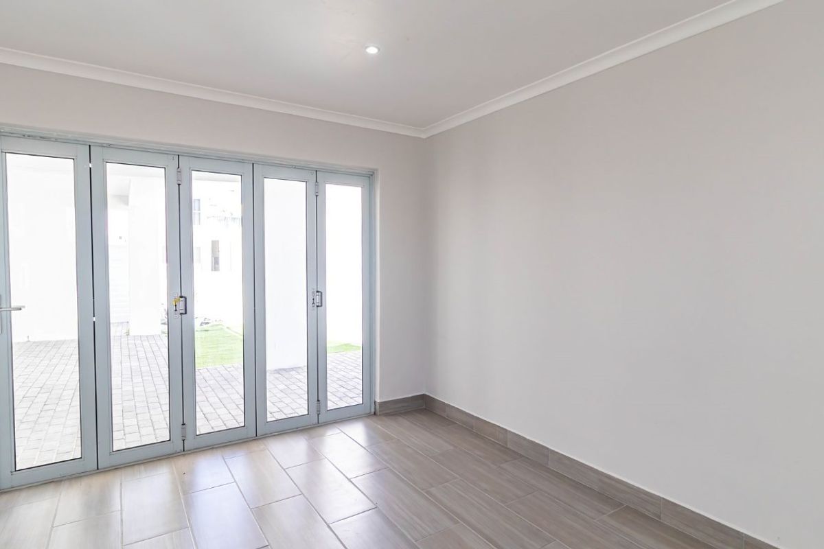 A bright, empty living area featuring neutral tiled flooring, crisp white walls, and large glass folding doors that open to an outdoor patio space.