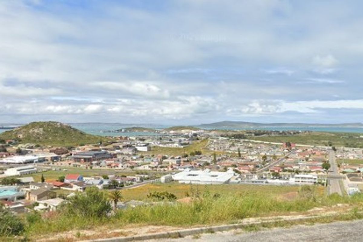 An elevated aerial view overlooking the surrounding residential neighborhood, coastal landscape, and distant hills, showcasing the property's scenic location.