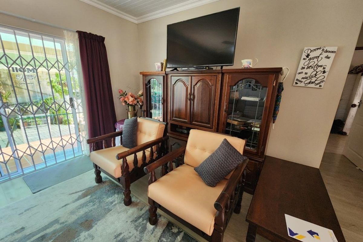 A living room area featuring a sliding glass door with security gate, wood-look flooring, and a tongue-and-groove ceiling finish.