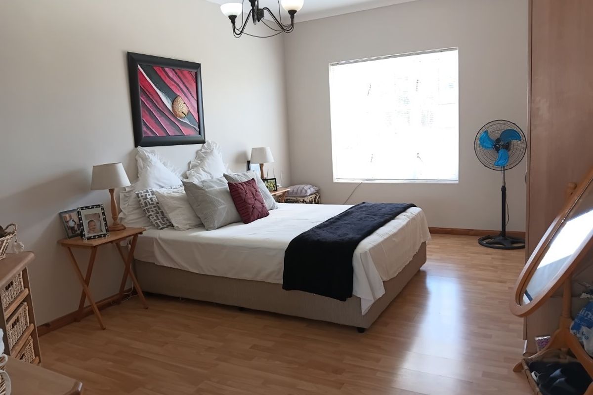 A well-lit bedroom featuring laminate wood flooring, neutral walls, and a classic chandelier light fixture.