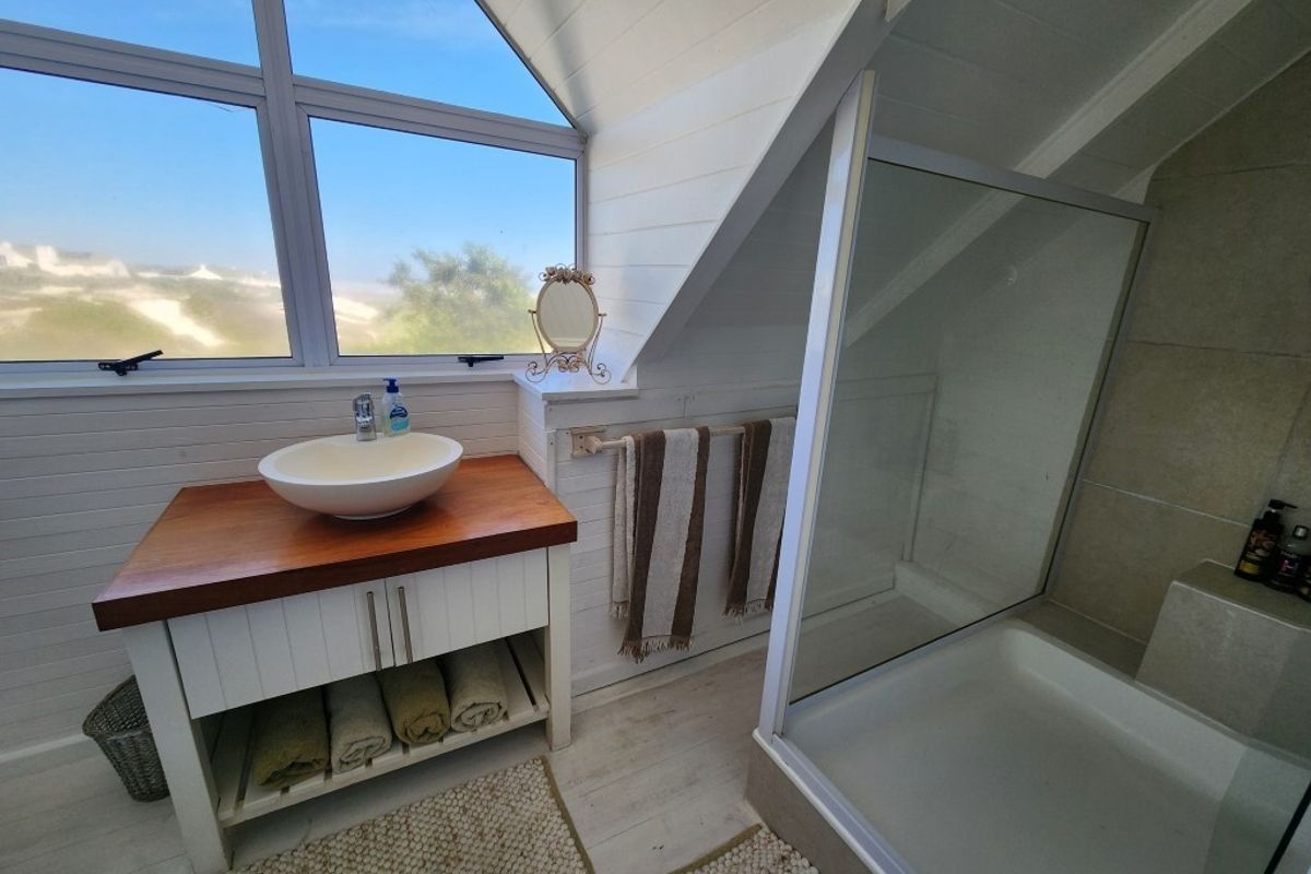 A bright bathroom featuring a vessel sink on a wooden vanity, a glass-enclosed shower, and timber wall paneling under a sloped ceiling.
