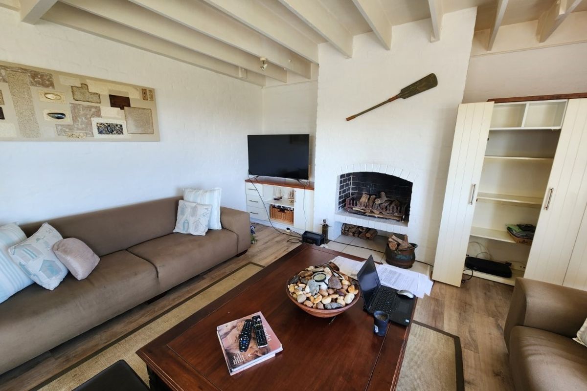 A cozy living room featuring a masonry fireplace, exposed beam ceiling, and built-in shelving, finished with durable laminate flooring.