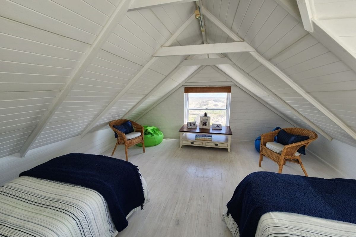 A charming attic bedroom featuring a pitched timber ceiling with exposed beams, painted timber flooring, and a window offering scenic views.